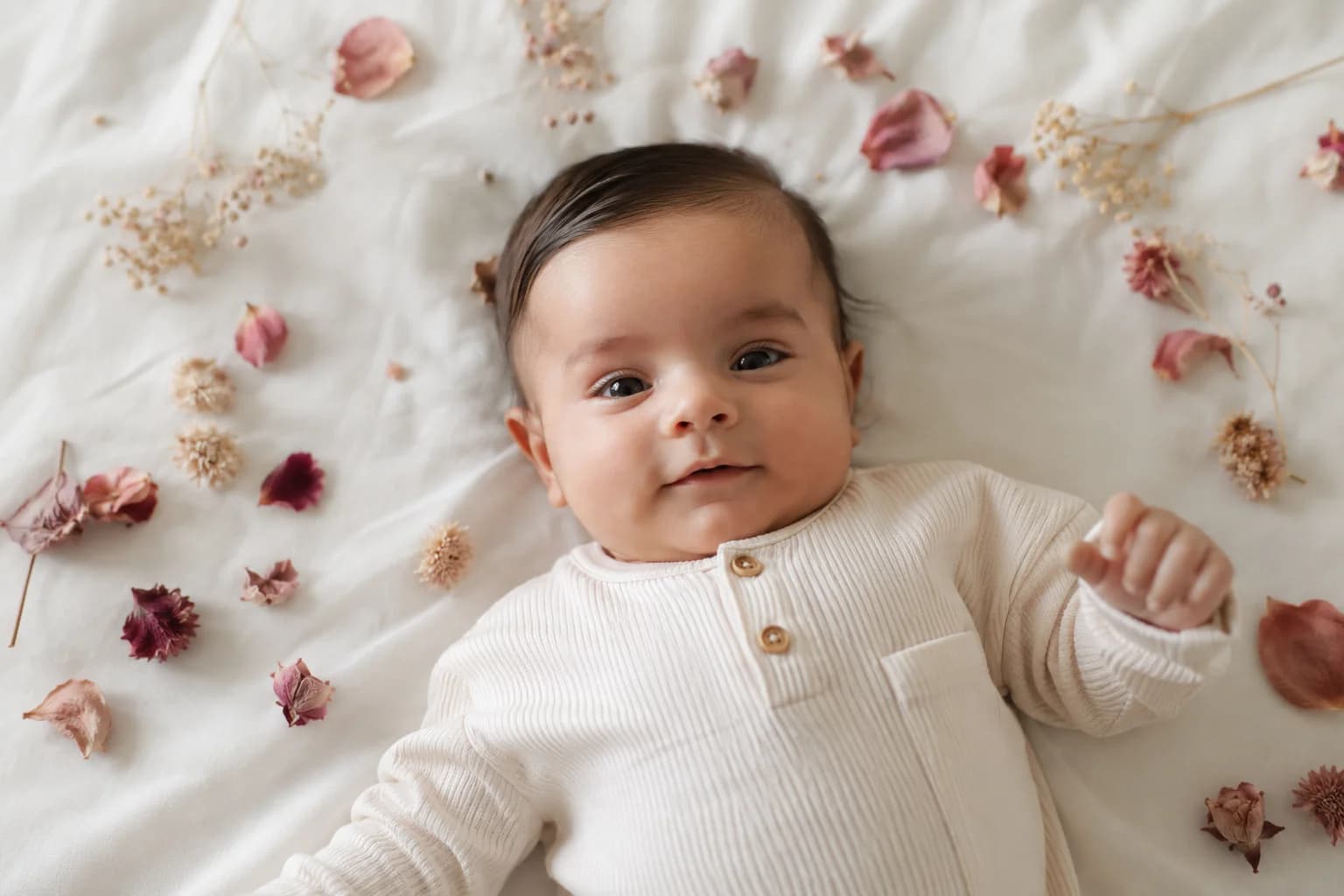 Bébé de 3 mois allongé sur du coton blanc entouré de fleurs séchées et pétales de roses roses et mauves